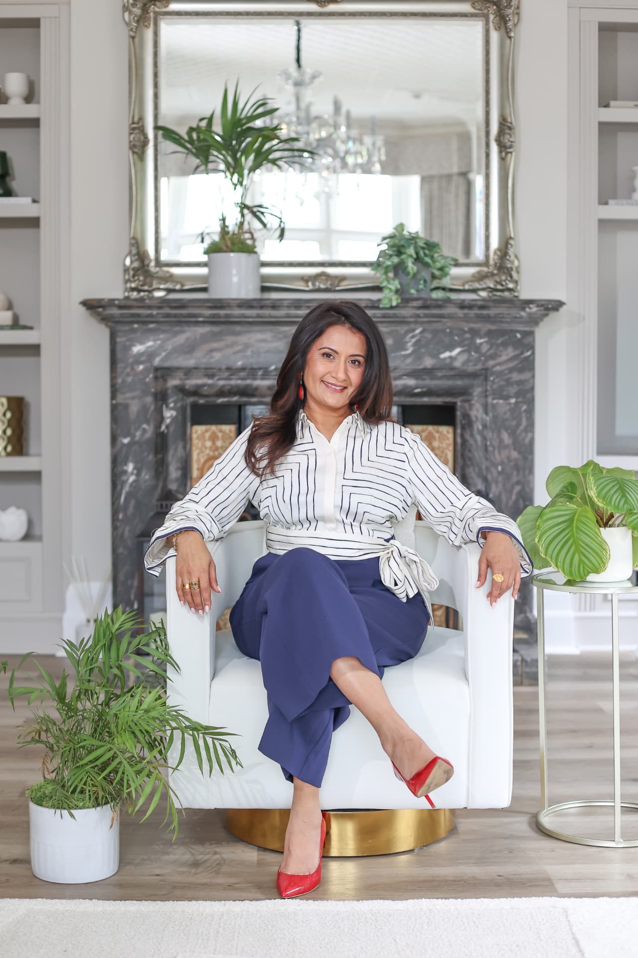 Kajal seated in a bright, elegant room with a marble fireplace and houseplants, smiling warmly at the camera.